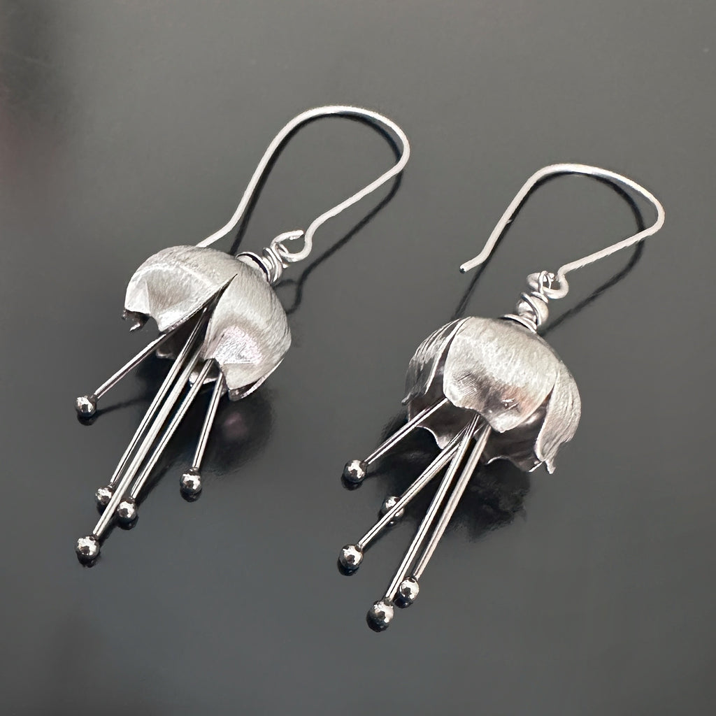 Hand made and scuplted surgical grade steel inverted flower pendant with a satin finish with long dangling stamen. Hanging from a long shepherds hook ear wires.