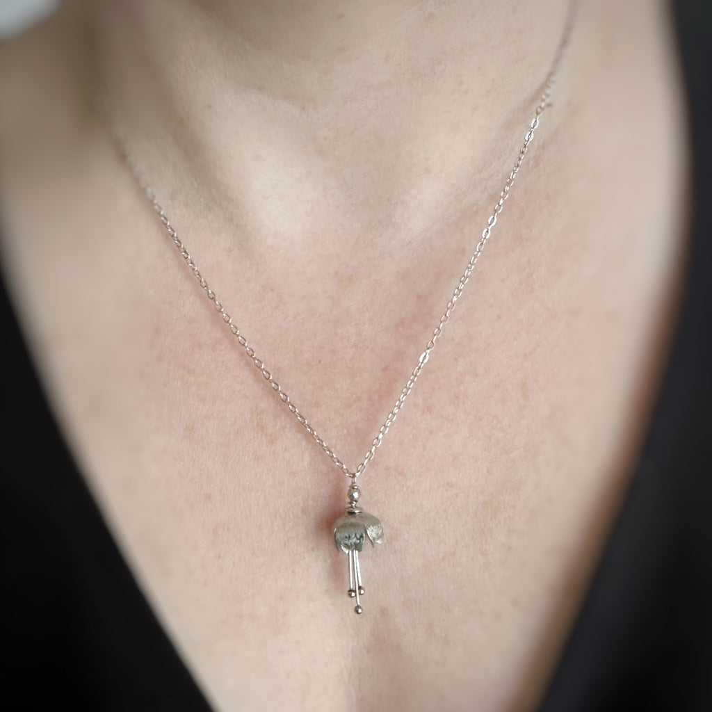 Hand made and scuplted surgical grade steel flower with a satin finish. The pendant hangs from a delicate chain. Shown on model.