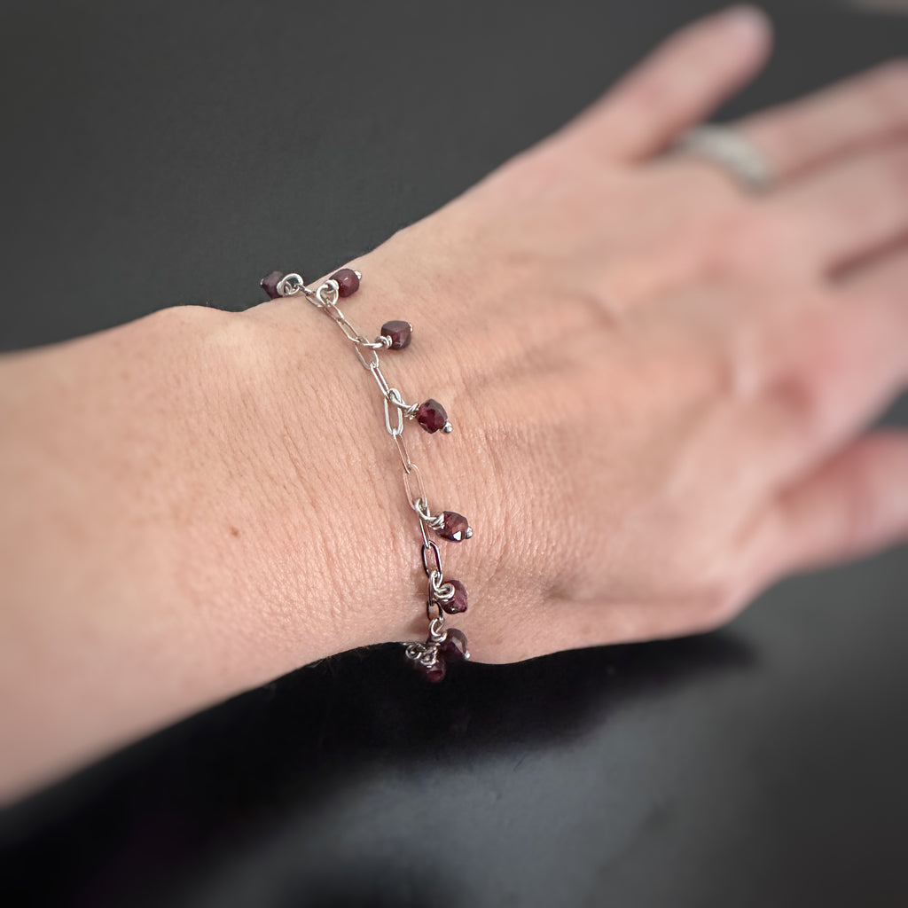 faceted cube shaped garnet beads dangling from a paper clip style silver tone chain. Shown on model.