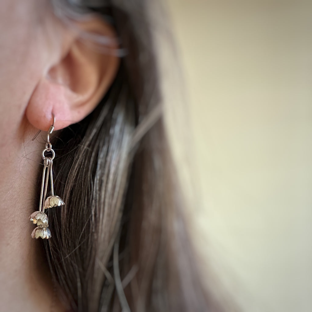Three tiny bell shaped flowers made from vintage silverplate, each on separate stems and hanging in a cluster from french hook style ear wire. Shown on model.