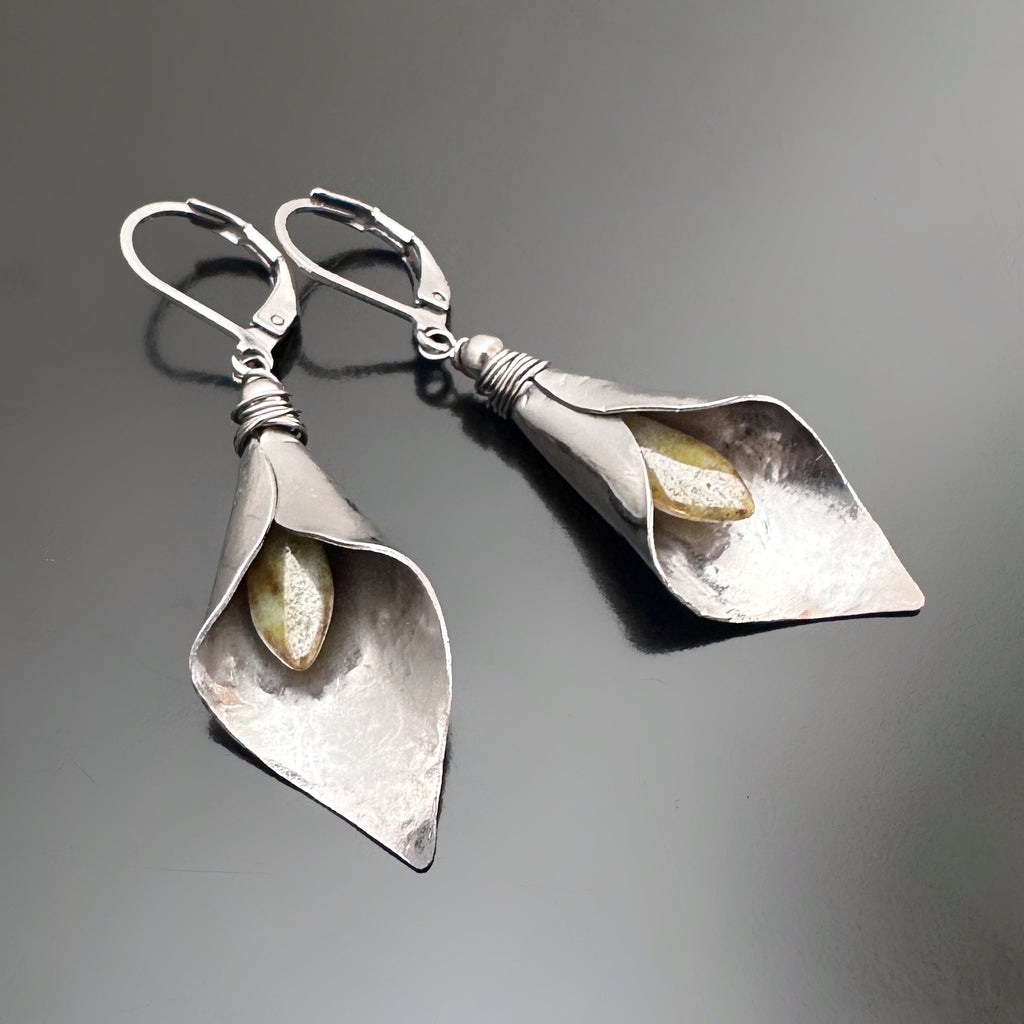 Hand formed silver tone surgical steel inverted calla lily drop earrings with pale green Czech glass stamen. The earrings use lever-back style ear wires.
