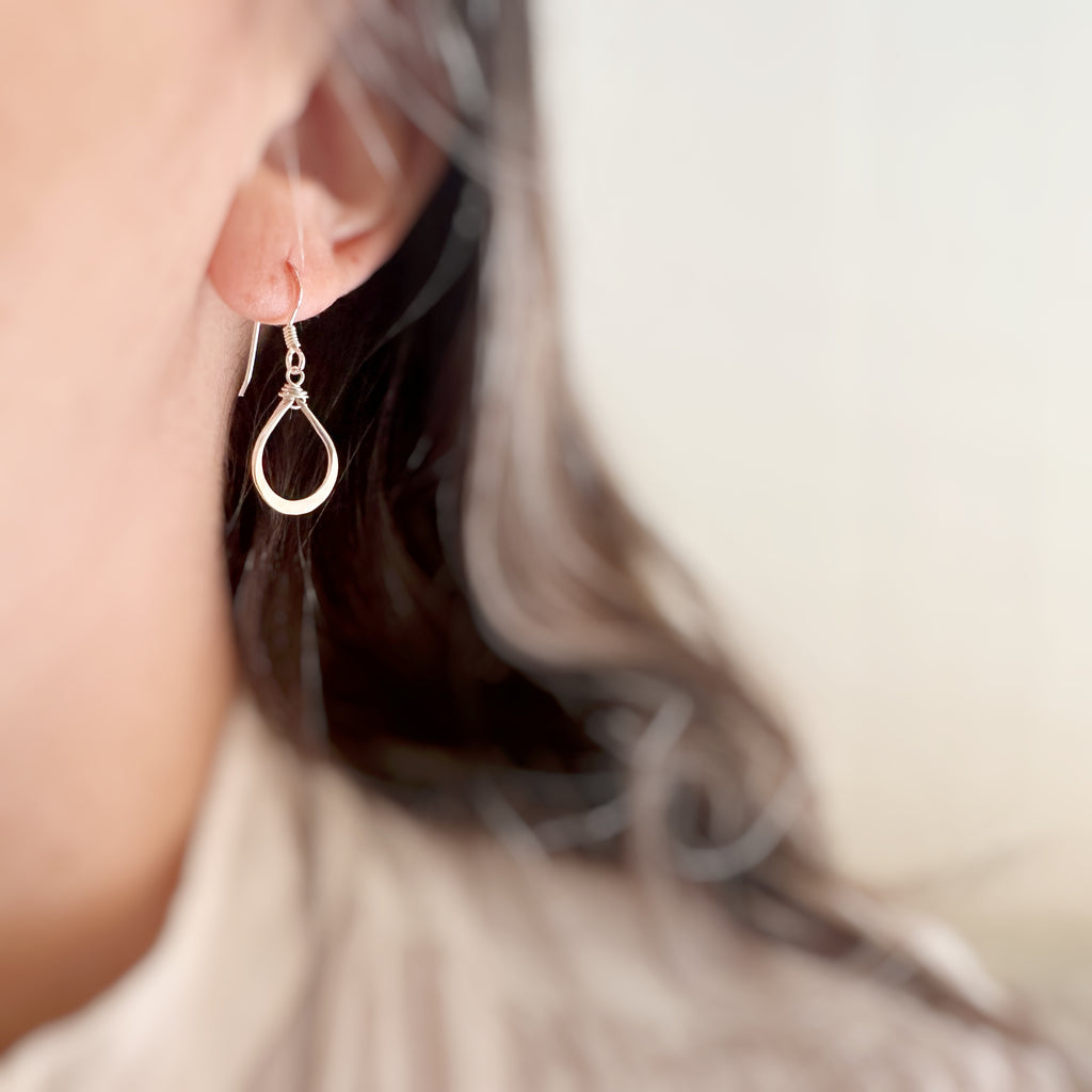 Close-up of a silver teardrop earring worn by a person with blurred background