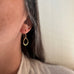 Close-up of a person wearing a gold hand hammered teardrop earring with a plain background