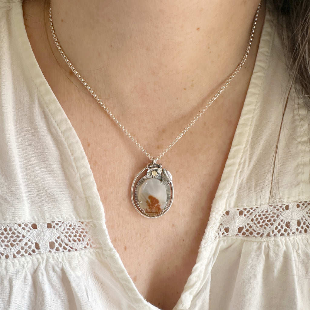 Handmade sterling silver pendant with a dendritic agate stone that has the appearance of a scene depicting a tree, field and sky. It also features a hand sculpted leaf and little 14k-gold-filled sun at the top.