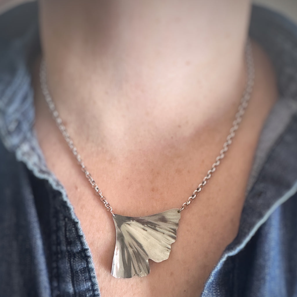 Silver surgical steel rolo chain necklace with a ginkgo leaf pendant worn by a person.