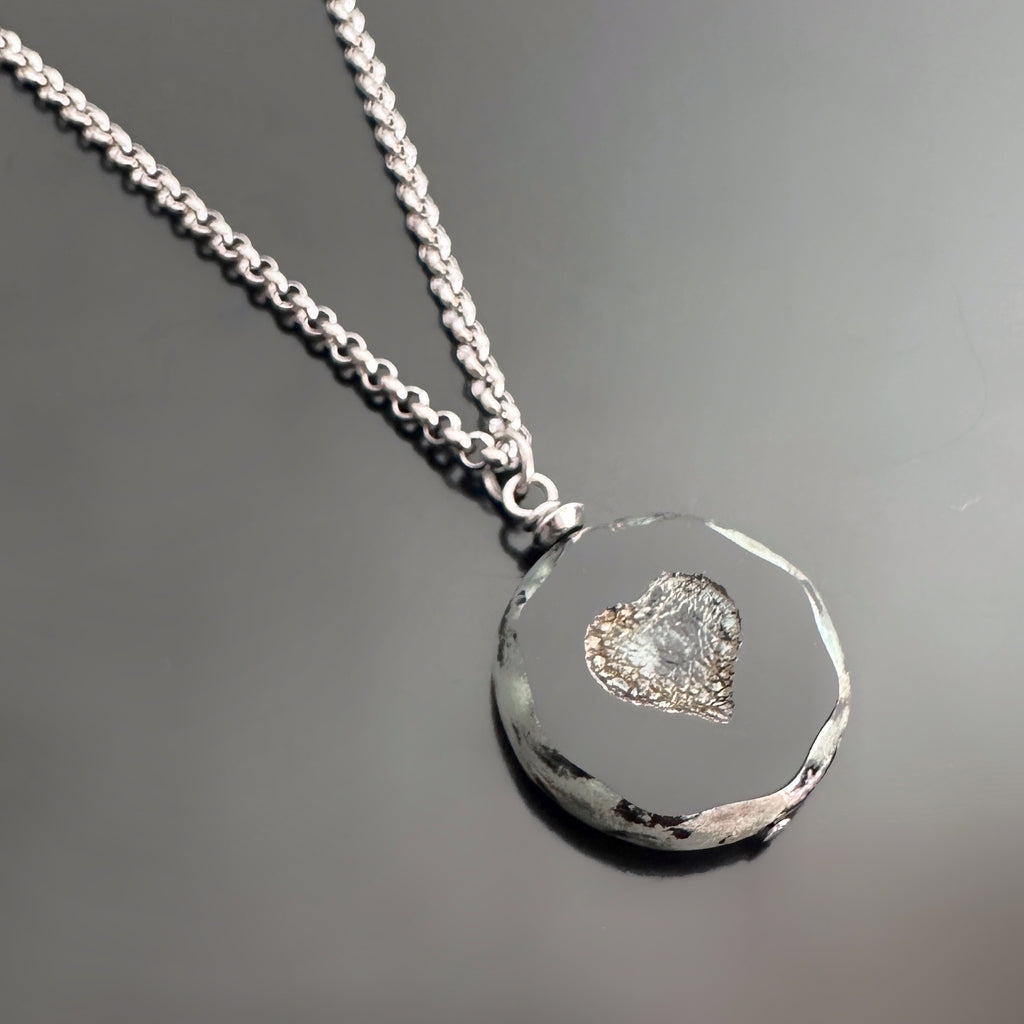Pendant necklace with a black glass coin shaped bead with crackled golden hearts in the center. The surgical steel chain is a rolo-style link.