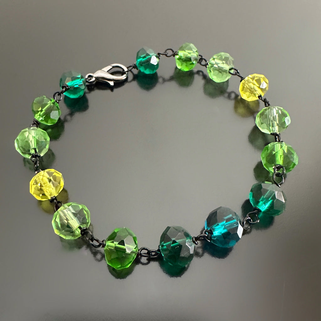 Green and yellow spectrum faceted glass beaded bracelet ,with hand wrapped, secure links, displayed on a table.