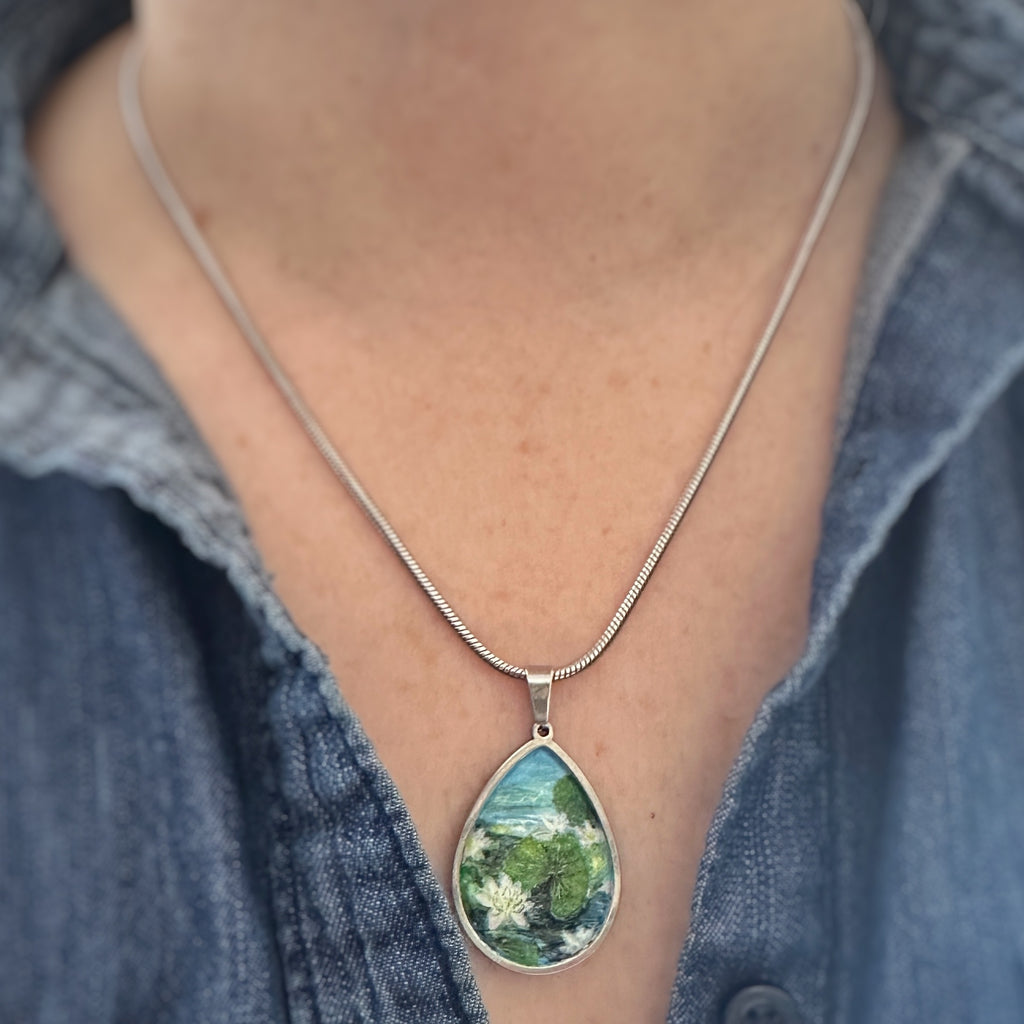 teardrop shaped pendant with a hand painted scene of water lilies on a pond. shown on a person.