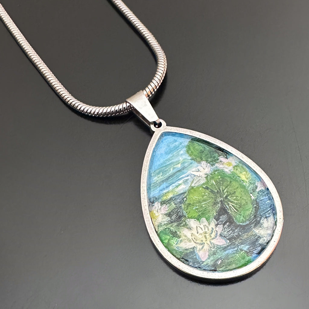 teardrop shaped pendant with a hand painted scene of water lilies on a pond.