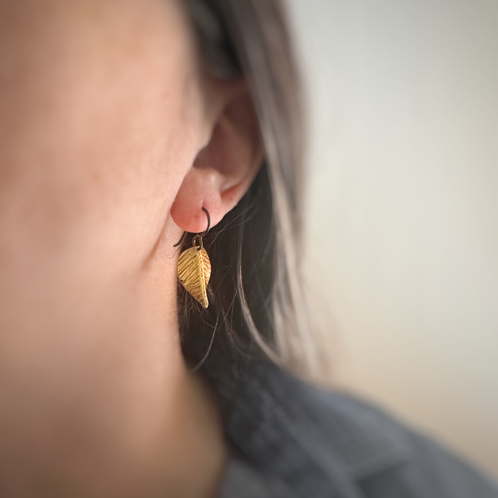 small earrings that are hand formed and hammer textured leaves made of oxidized brass
