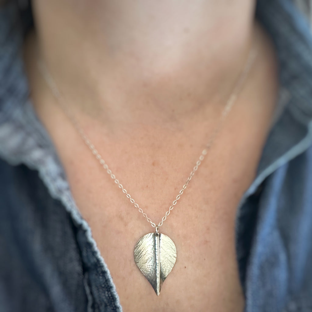 Extra large, silver leaf-shaped pendant on a delicate chain necklace show being worn.