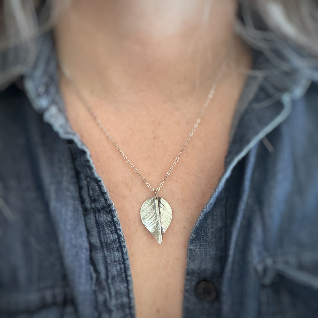 Large, silver leaf-shaped pendant on a delicate chain necklace show being worn.