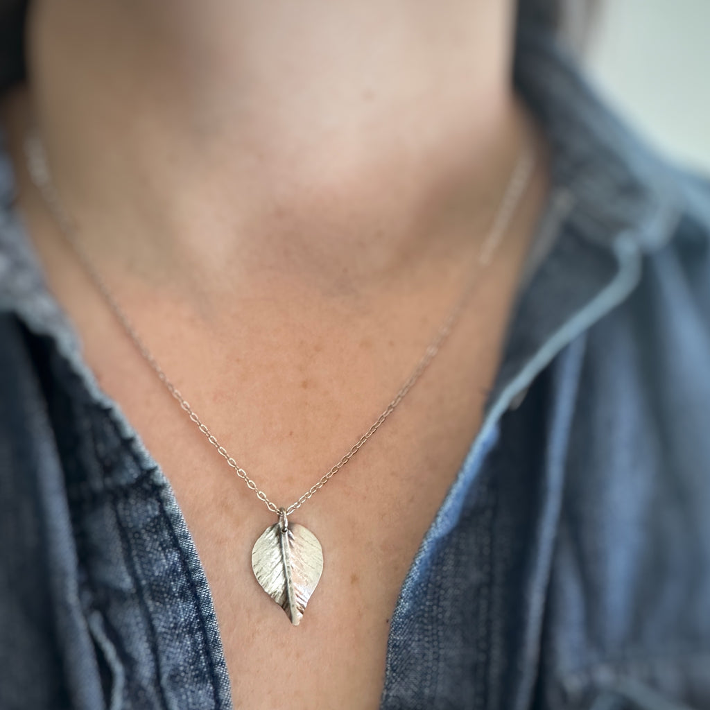 Medium, silver leaf-shaped pendant on a delicate chain necklace show being worn.