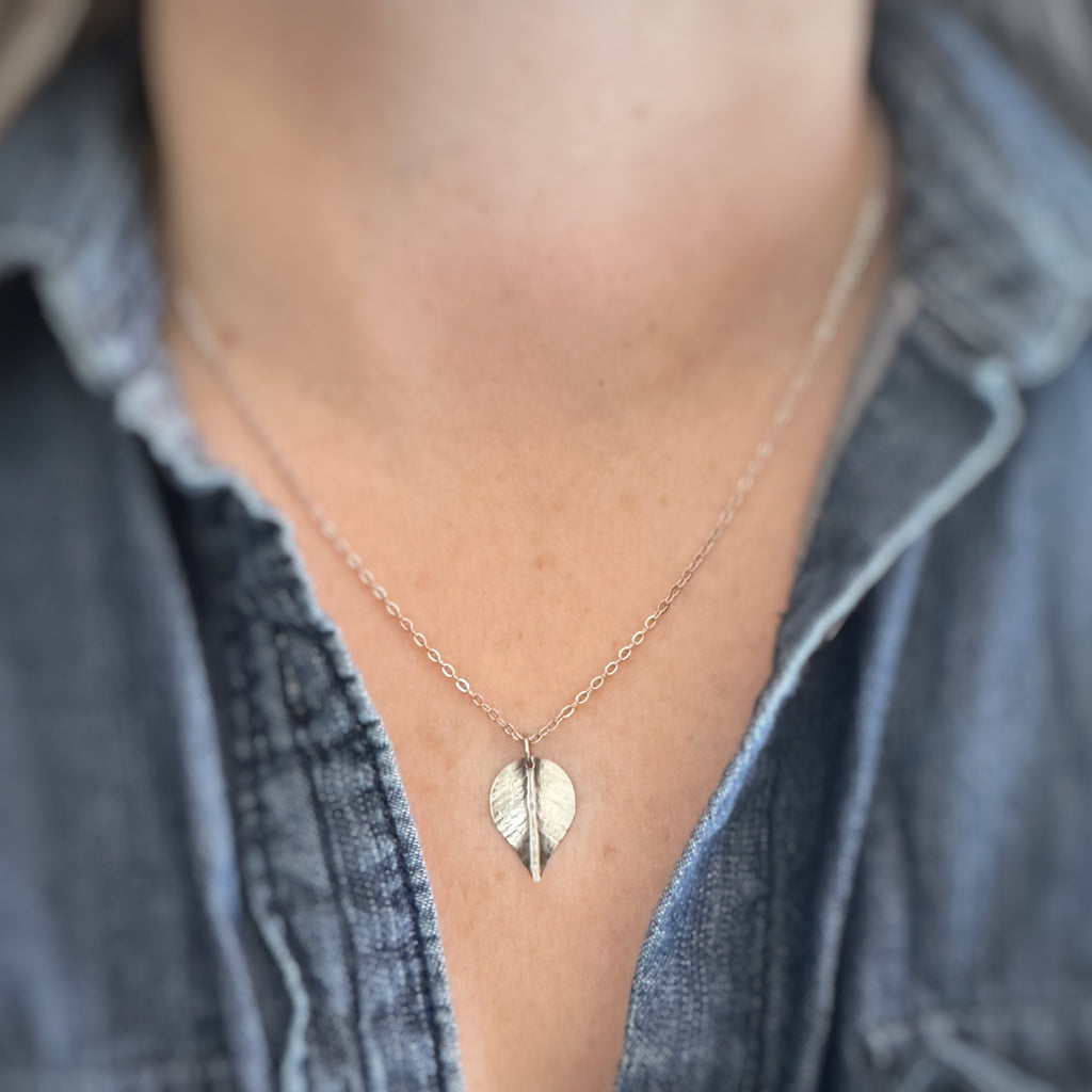 Small, silver leaf-shaped pendant on a delicate chain necklace show being worn.