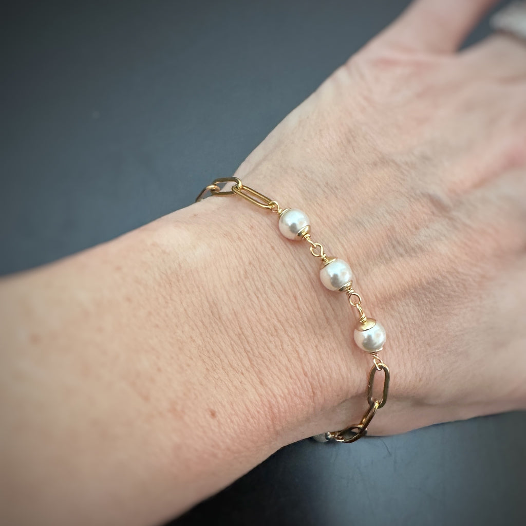 6mm white crystal pearls linked in groups of three interspersed within a gold tone paperclip style chain. shown as worn.