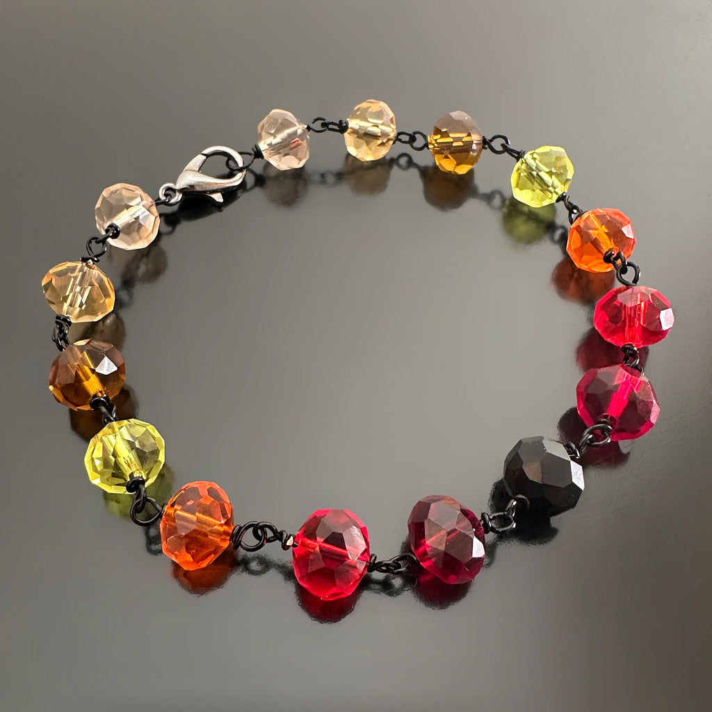 yellow, orange and red spectrum faceted glass beaded bracelet ,with hand wrapped, secure links, displayed on a table.