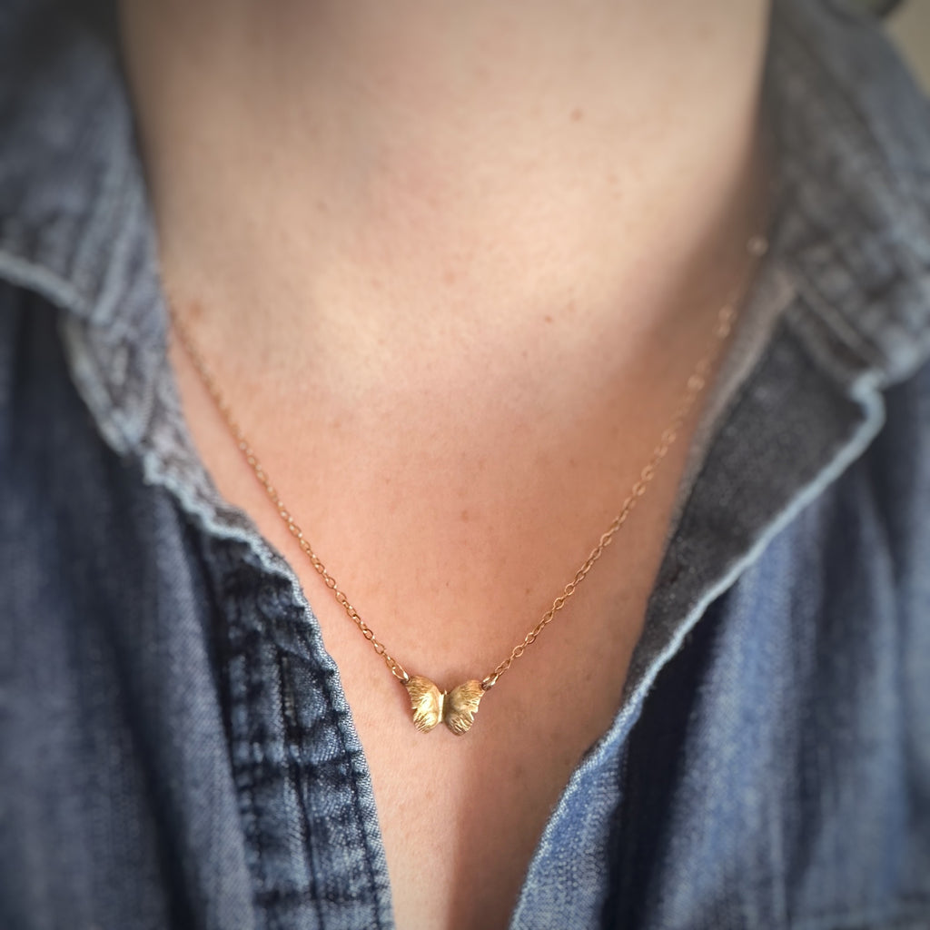 Petite golden brass necklace with a butterfly pendant worn by a person wearing a denim shirt.