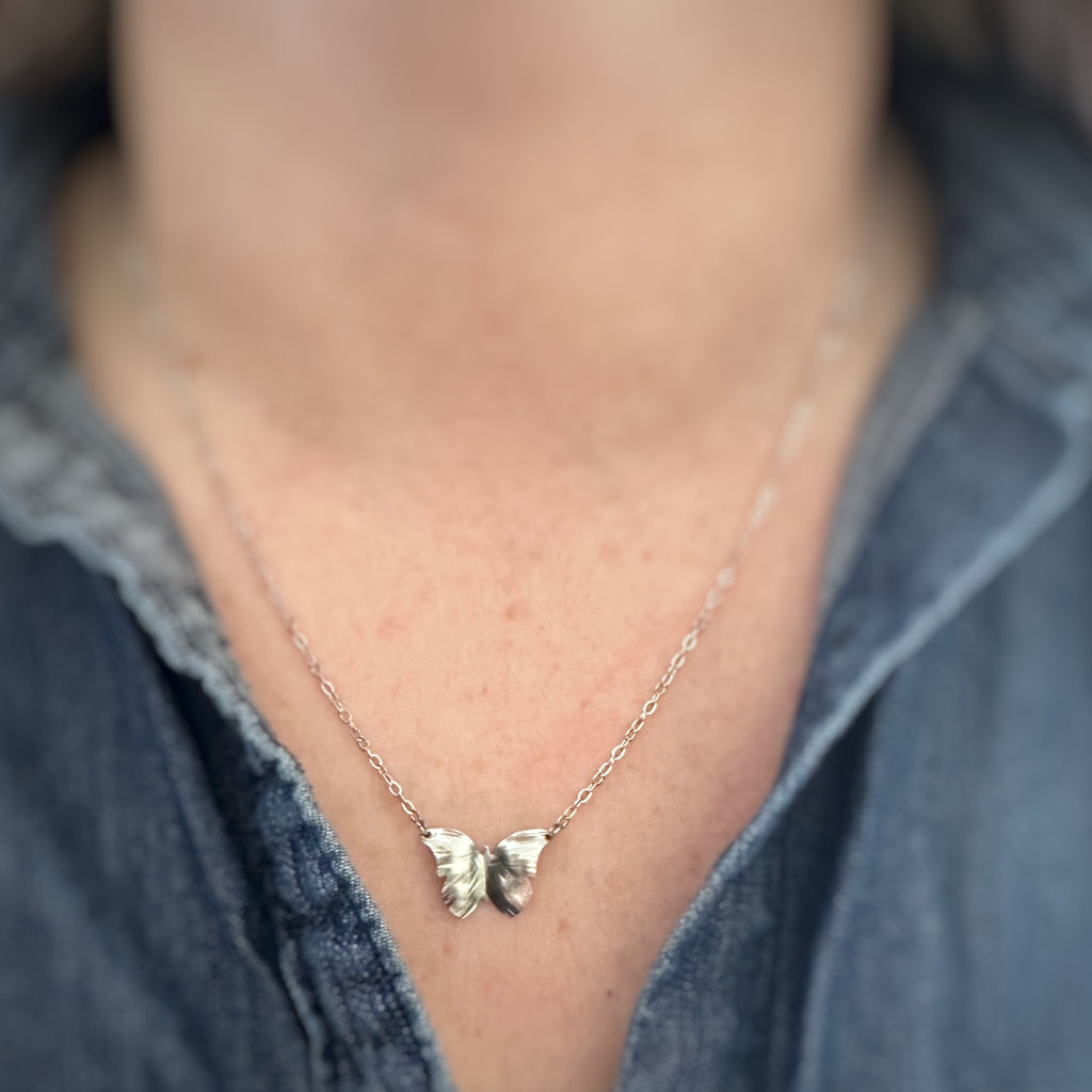 silver tone surgical steel butterfly pendant with hammered details in the wings, on a dainty chain. shown as worn.