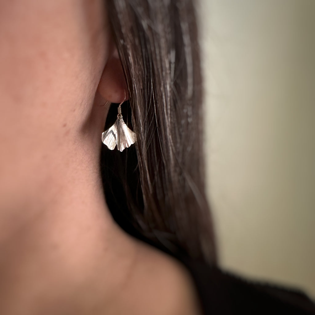 Small sterling silver ginkgo leaf earrings on model.
