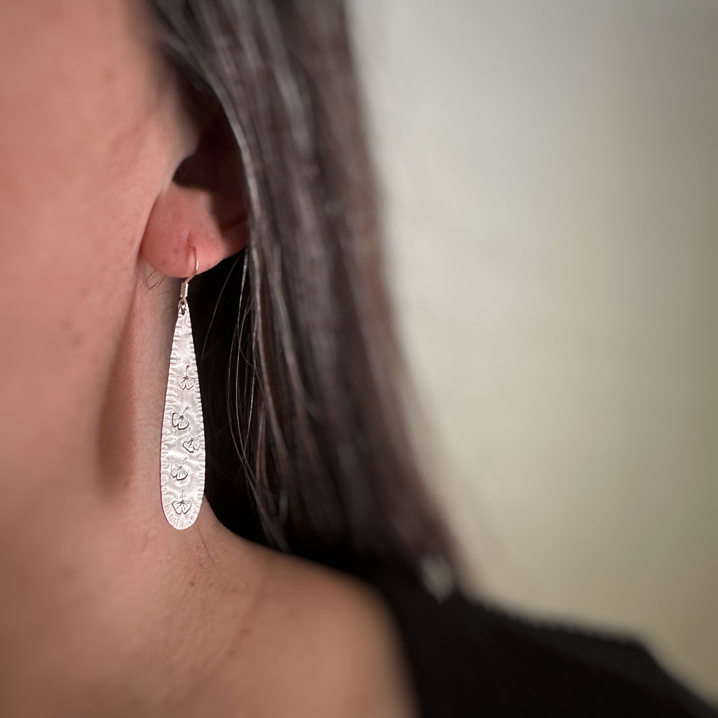 Sterling silver teardrop earrings with stamped ginkgo leaves on model.
