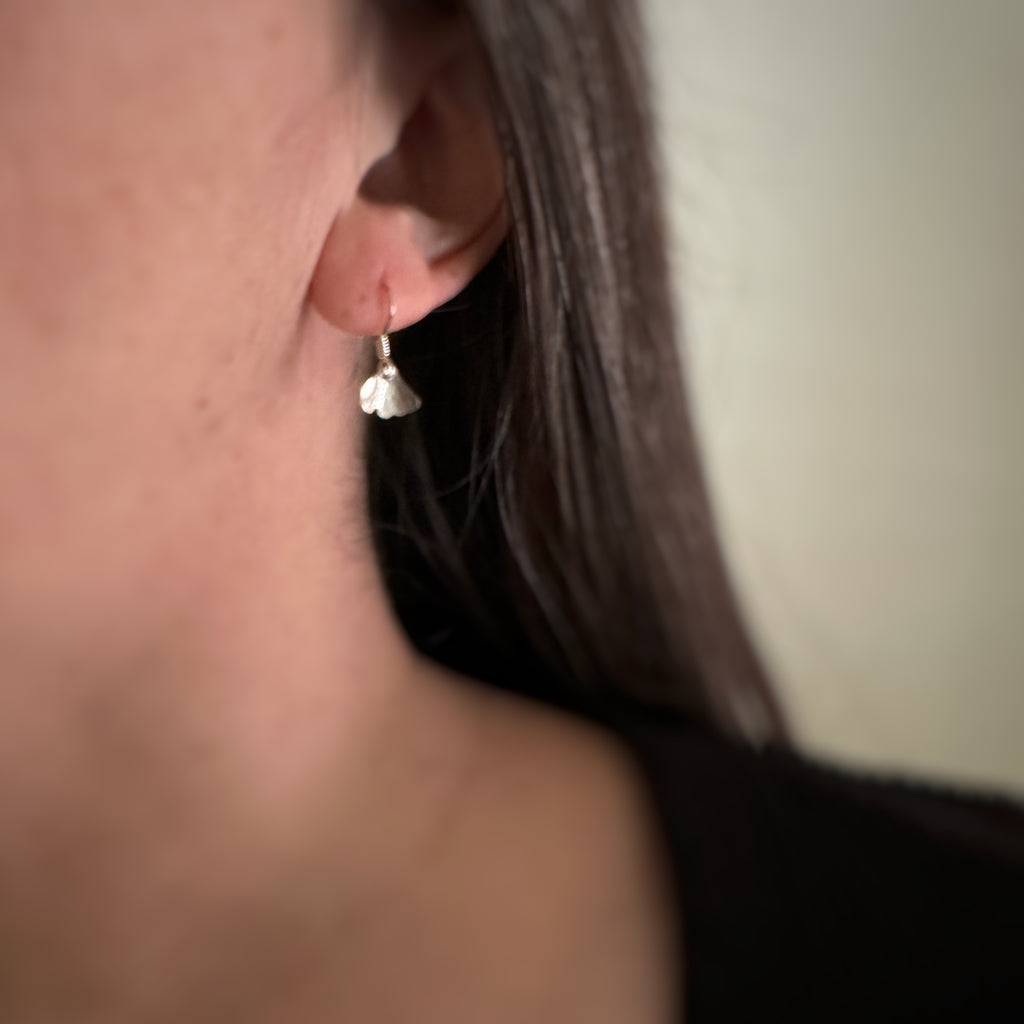 Tiny sterling silver ginkgo leaf earrings on model.