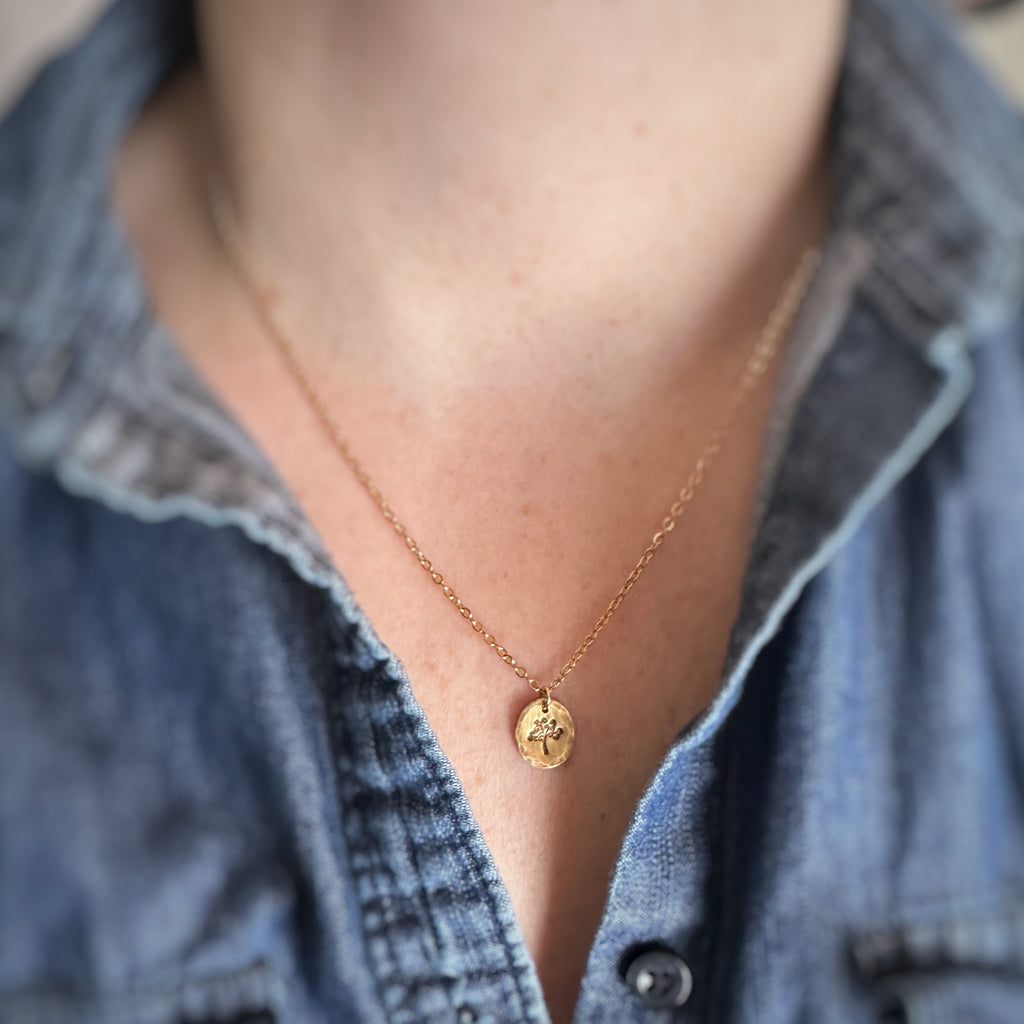 Gold antiqued brass necklace with an oval pendant with a hammered texture depicting a swirly tree.