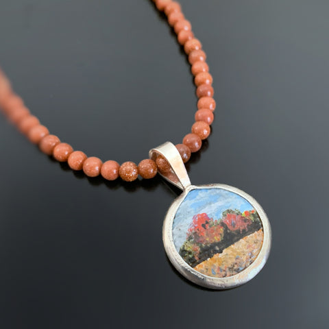 Hand painted sterling silver pendant depicting a forest edge in Autumn on a goldstone beaded chain.