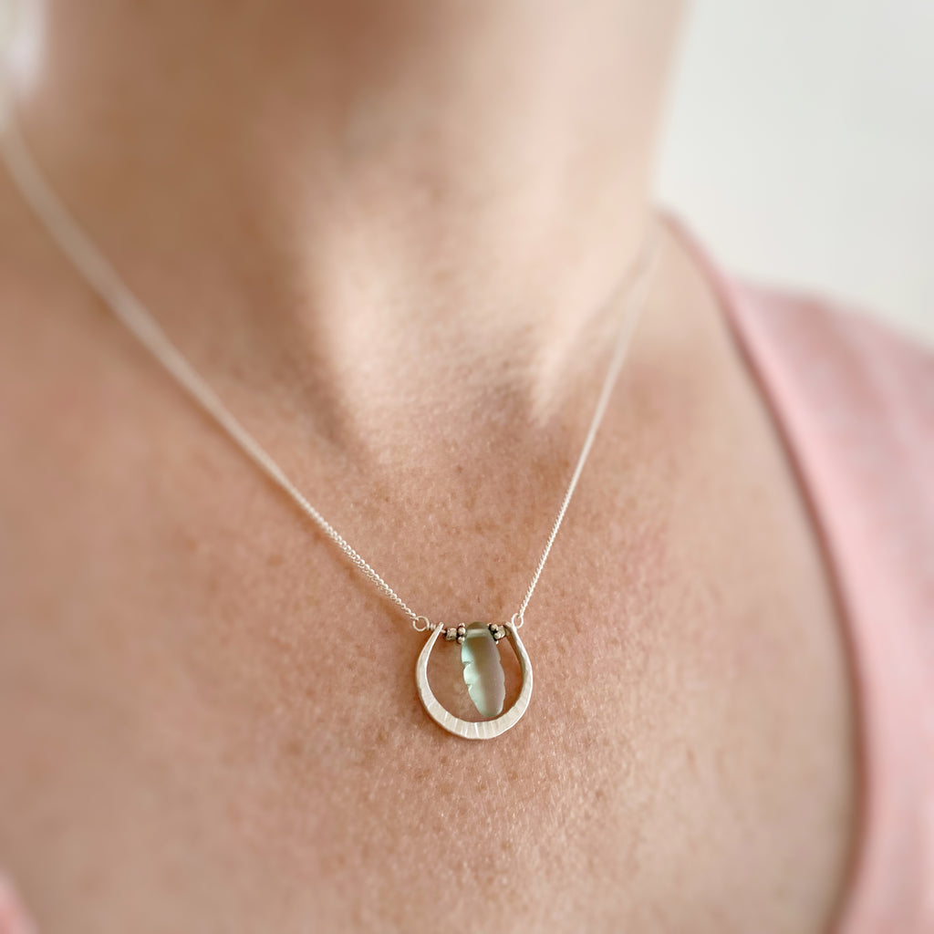 Handmade sterling silver U shaped pendant with a frosted green glass dagger shown on model.