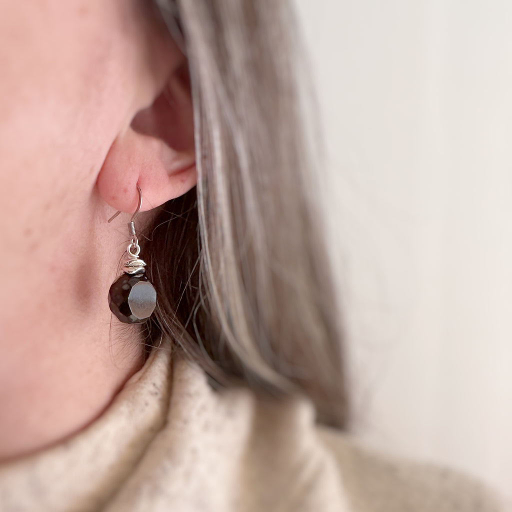 Black glass faceted nugget drop earrings with silvery accents and surgical steel ear wires. Shown on model.