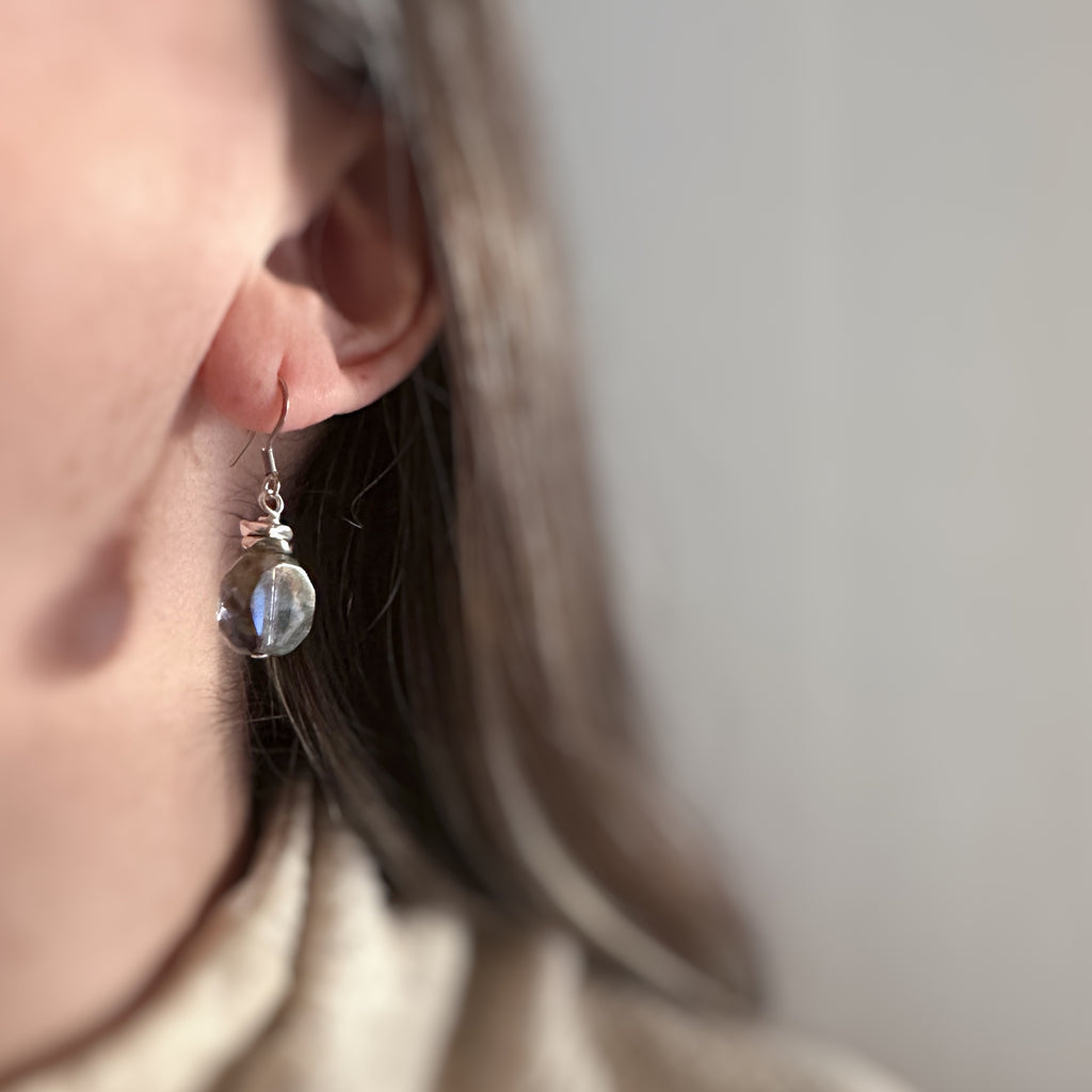 Earthy blue, transparent glass faceted nugget drop earrings with silvery accents and surgical steel ear wires. Shown on model.