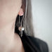 Hand made and scuplted surgical grade steel inverted flower pendant with a satin finish with  long dangling stamen. Hanging from a long shepherds hook ear wires. Shown on model.