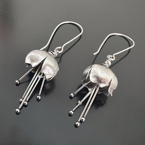 Hand made and scuplted surgical grade steel inverted flower pendant with a satin finish with  long dangling stamen. Hanging from a long shepherds hook ear wires.