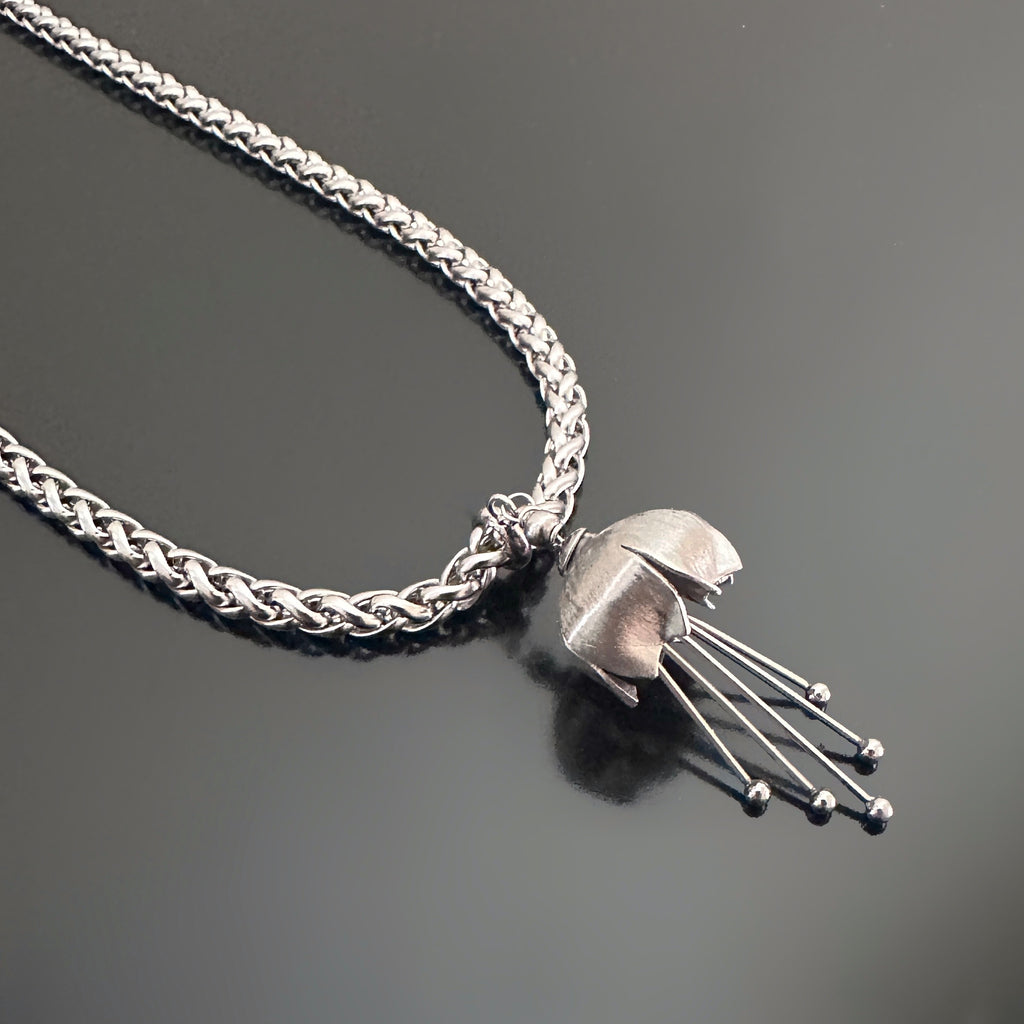 Hand made and scuplted surgical grade steel inverted flower pendant with a satin finish with  long dangling stamen. Hanging from a thick chain necklace.