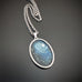 Silver color oval shaped pendant, hand painted depicting a full moon in a dark but hazy sky, and a row of trees on the left side.
