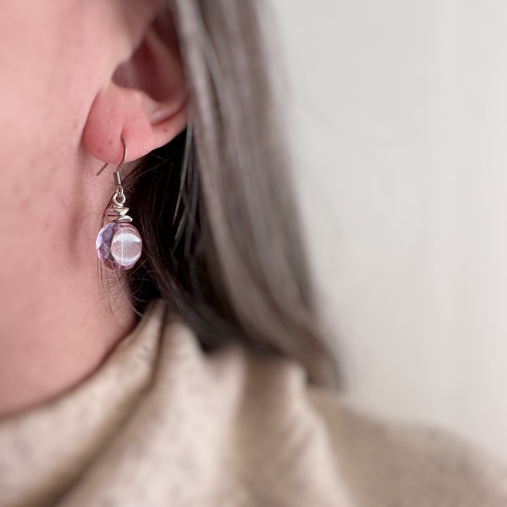 Purple lilac transparent glass faceted nugget drop earrings with silvery accents and surgical steel ear wires. Shown on model.