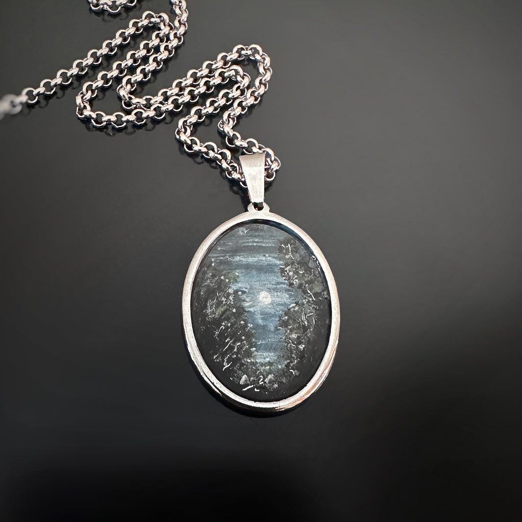 Silver colored oval shaped pendant, hand painted, depicting trees in the moonlight.