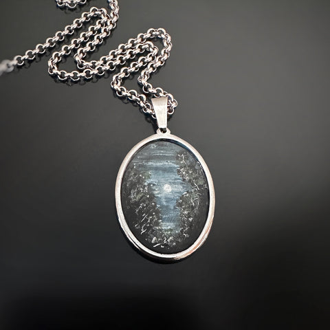 Silver colored oval shaped pendant, hand painted, depicting trees in the moonlight.