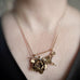 Golden brass and surgical steel pendant necklace, evoking a leaf filled bouquet highlighting a peony and a tiny wild rose with a small moonstone and hanging asymmetrically from a rolo style chain. Shown on model with 18inch chain.