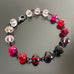 pink and red spectrum faceted glass beaded bracelet ,with hand wrapped, secure links, displayed on a table.