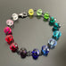 A collection of rainbow spectrum faceted glass beaded bracelets in various colors, with hand wrapped, secure links, displayed on a table.