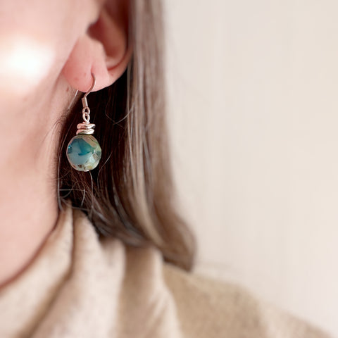 Swirly turquoise glass faceted nugget drop earrings with silvery accents and surgical steel ear wires. Shown on model.