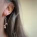 Three tiny bell shaped flowers made from vintage silverplate, each on separate stems and hanging in a cluster from french hook style ear wire. Shown on model.