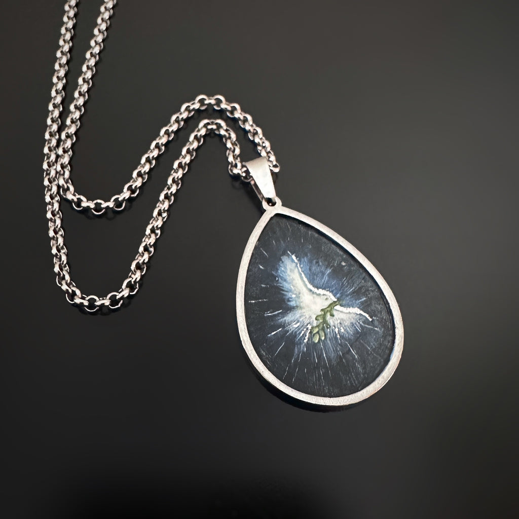 Silver color teardrop shaped pendant, hand painted depicting a white dove carrying an olive brance and set against a midnight blue sky.