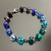 Blue and aqua spectrum faceted glass beaded bracelet ,with hand wrapped, secure links, displayed on a table.