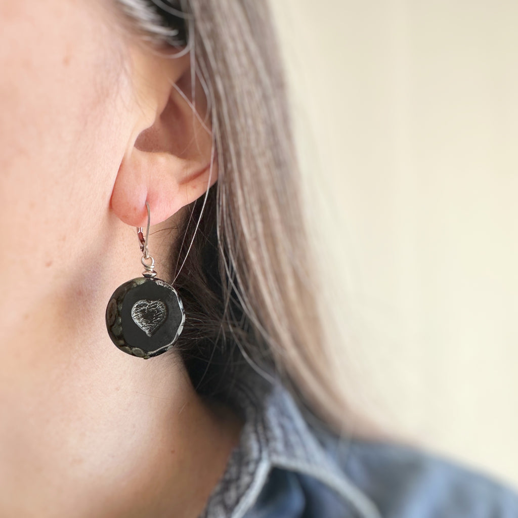 lever-back style earrings with black color glass coin shaped beads with crackled golden hearts in the center. 