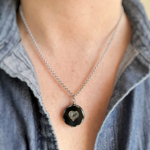 Pendant style necklace with a black glass coin shaped bead with crackled golden hearts in the center. The surgical steel chain is a rolo-style link.