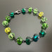 Green and yellow spectrum faceted glass beaded bracelet ,with hand wrapped, secure links, displayed on a table.
