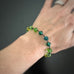 Green and yellow spectrum faceted glass beaded bracelet ,with hand wrapped, secure links, displayed on a table. shown worn on wrist