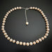 A hand knotted peach freshwater pearl necklace with an adjustable length, featuring pearl beads and a metallic clasp.
