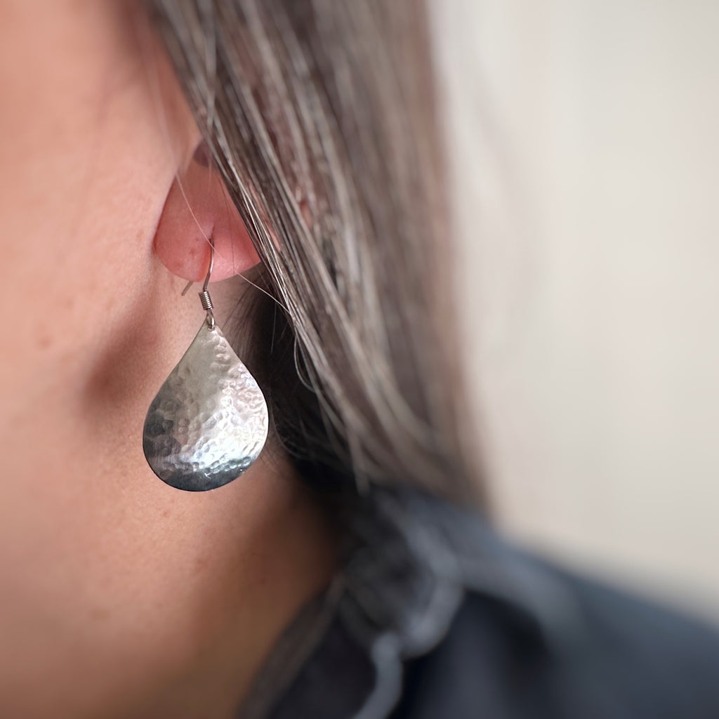 Large silvery teardrop dangle earrings with a subtle hammered texture. Shown as worn.